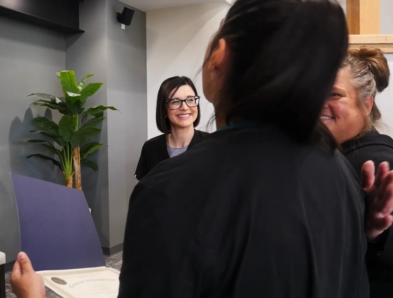 Photo of two dental professionals smiling at a mock student who is holding a certificate of completion